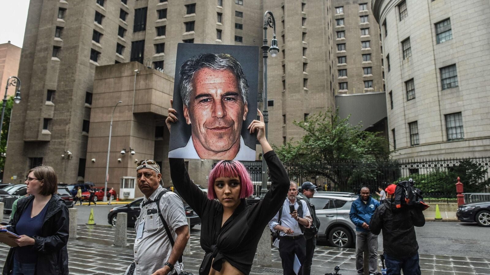 A member of a protest group called 'Hot Mess' holds up a sign of Jeffrey Epstein in front of the Metropolitan Correction Center.
