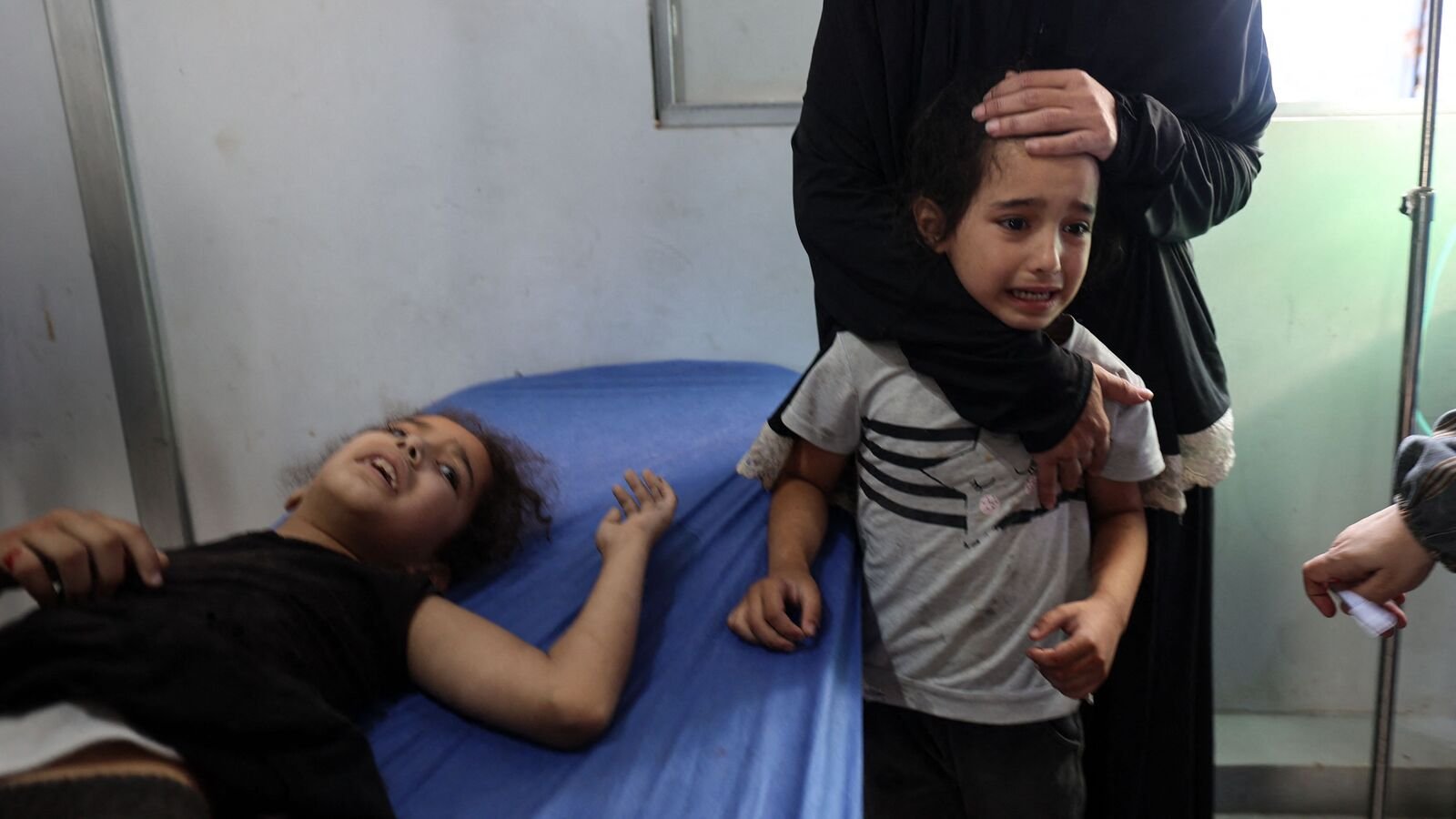 A Palestinian child reacts as she stands near a girl receiving treatment for his injuries at the Al-Awda hospital in Nuseirat in the central Gaza Strip, following Israeli strikes on July 13, 2025. Gaza's civil defence agency said Israeli air strikes on July 13 killed at least 29 Palestinians, including six children near a water distribution point. (Photo by Eyad BABA / AFP)