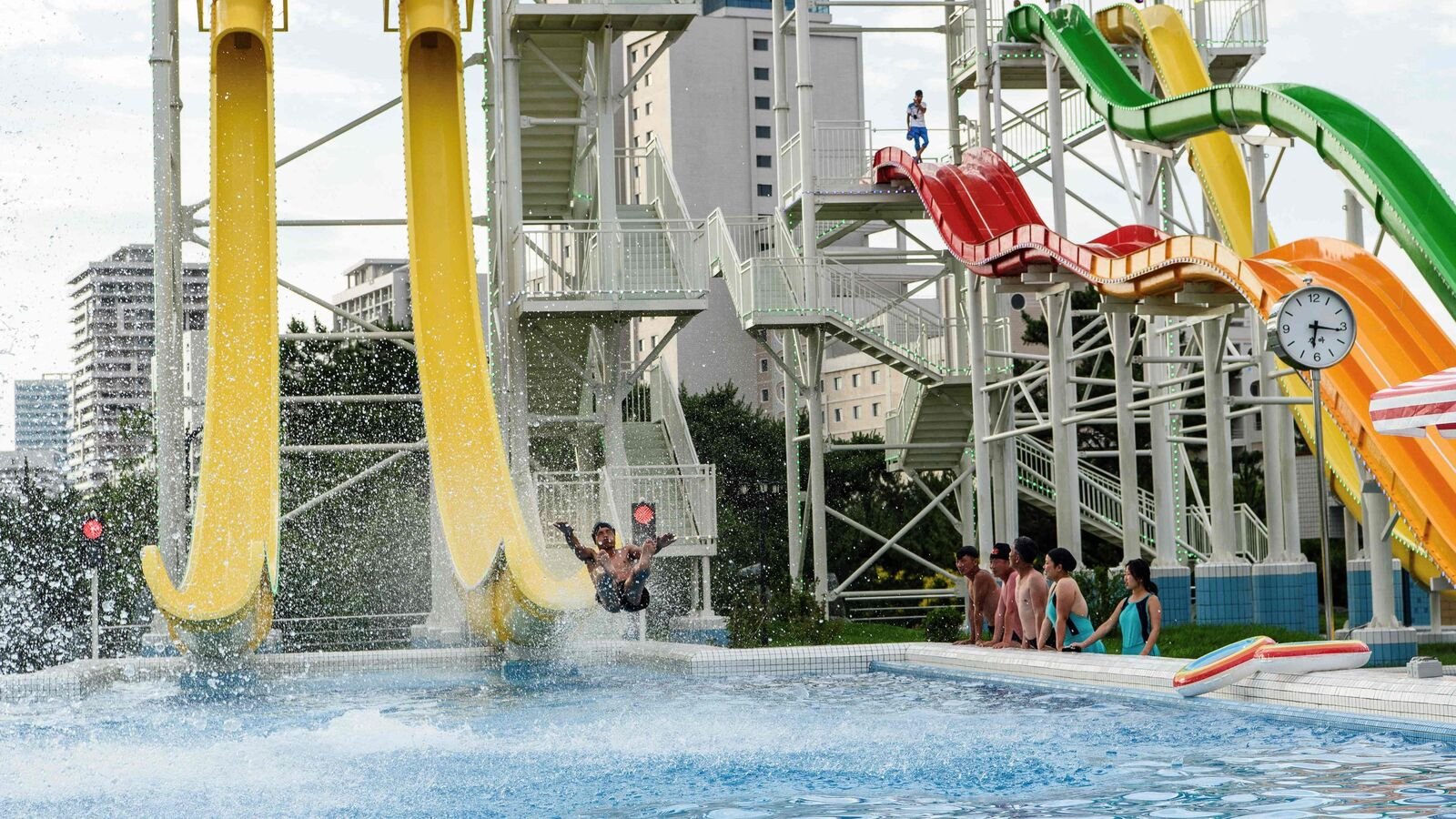 (FILES) Domestic tourists watch as a man uses a slide into a swimming pool at the Myongsasimni Water Park in the Wonsan Kalma Coastal Tourist Area in Wonsan, North Korea's Kangwon Province on July 2, 2025. (Photo by KIM Won Jin / AFP)