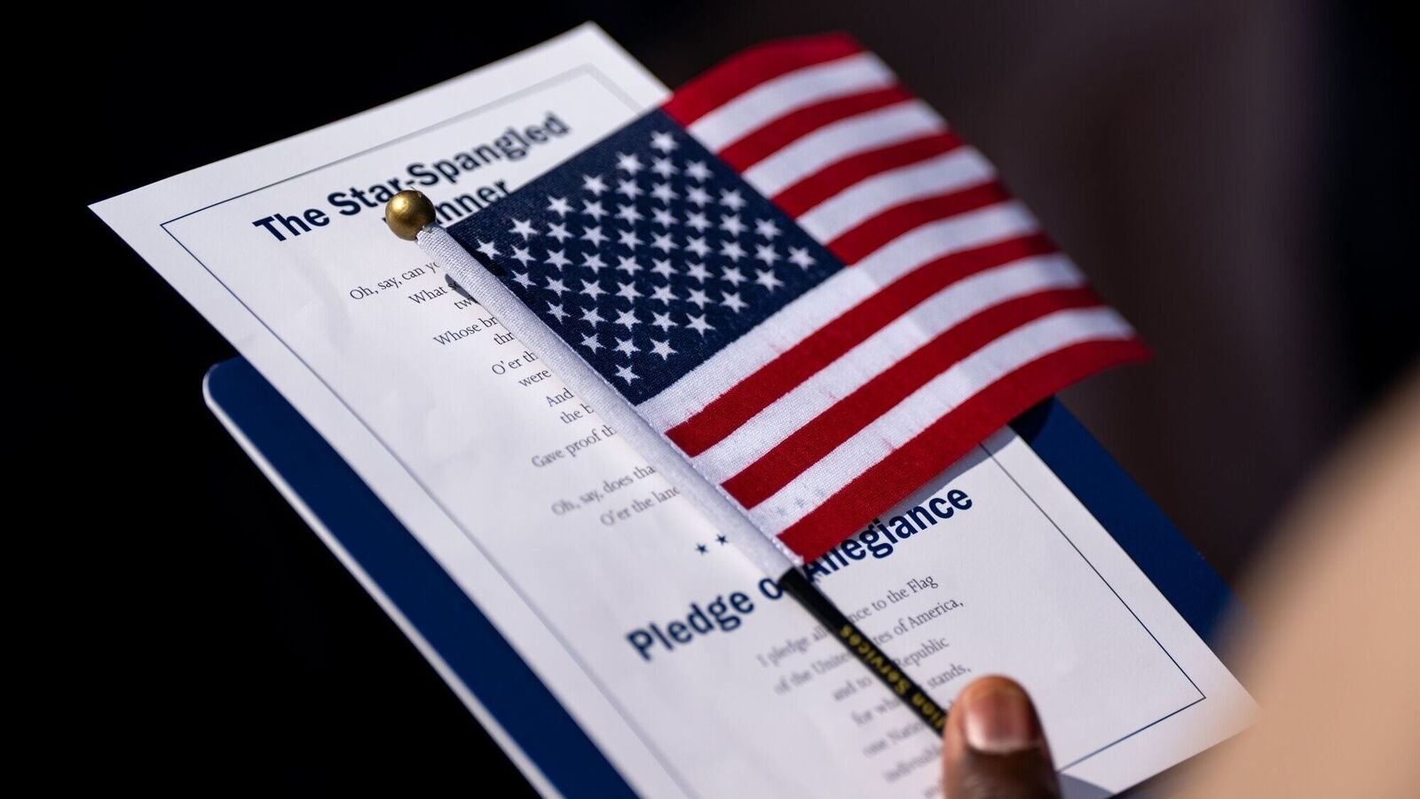 An attendee holds the US flag and the lyrics of the Star Spangled Banner during a naturalization ceremony at George Washington's Mount Vernon in Mount Vernon, Virginia, US, on Friday, July 4, 2025.
