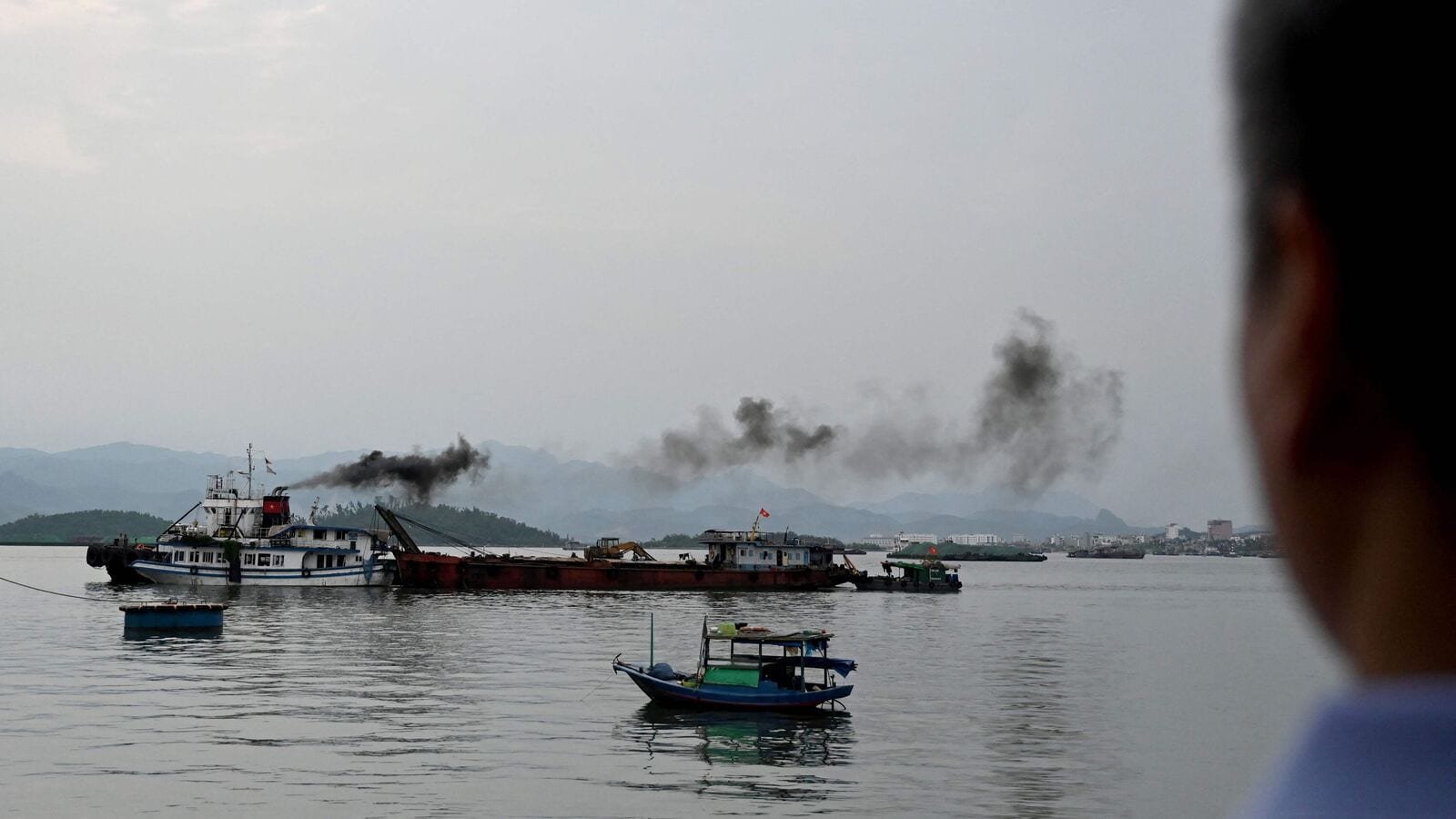 The tourist boat (front L) that capsized is towed back to the port in Ha Long bay, Quang Ninh province on July 20, 2025. A tourist boat ferrying families around Vietnam's Ha Long Bay capsized in a storm on on July 19 afternoon, leaving at least 34 people dead, according to state media reports, as rescuers scrambled to locate the missing. (Photo by Nhac NGUYEN / AFP)