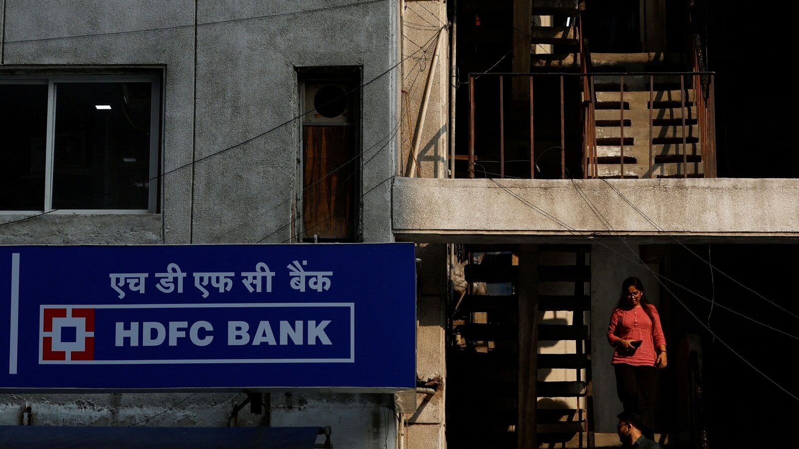 FILE PHOTO: A woman walks past a signboard of HDFC Bank's automated teller machine (ATM) in New Delhi, India, May 5, 2023. REUTERS/Anushree Fadnavis/File Photo