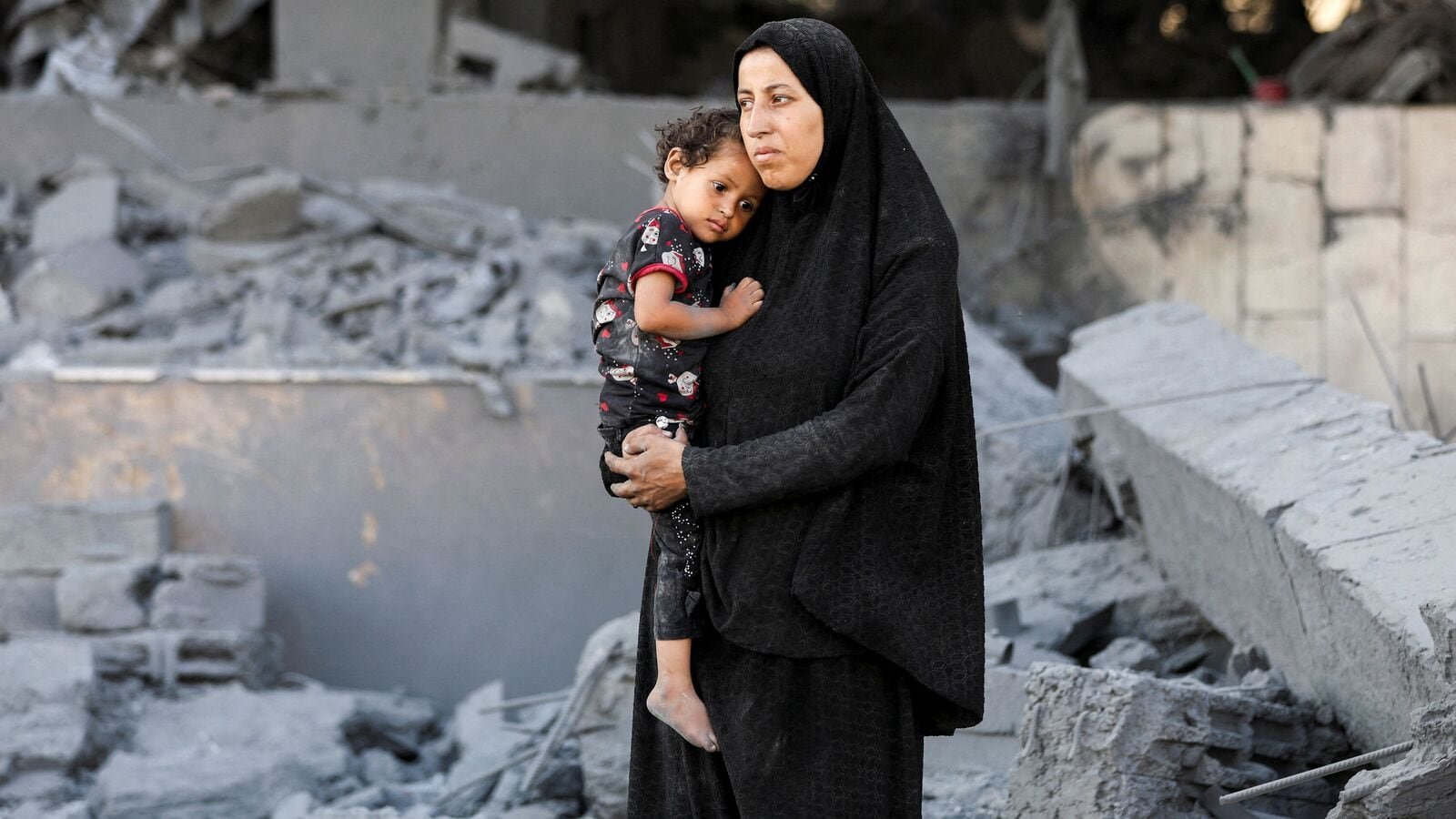 A Palestinian woman looks on holding a child at the site surrounding an evacuated UNRWA clinic where displaced people were taking shelter, following an overnight Israeli strike, in Gaza City August 6, 2025.