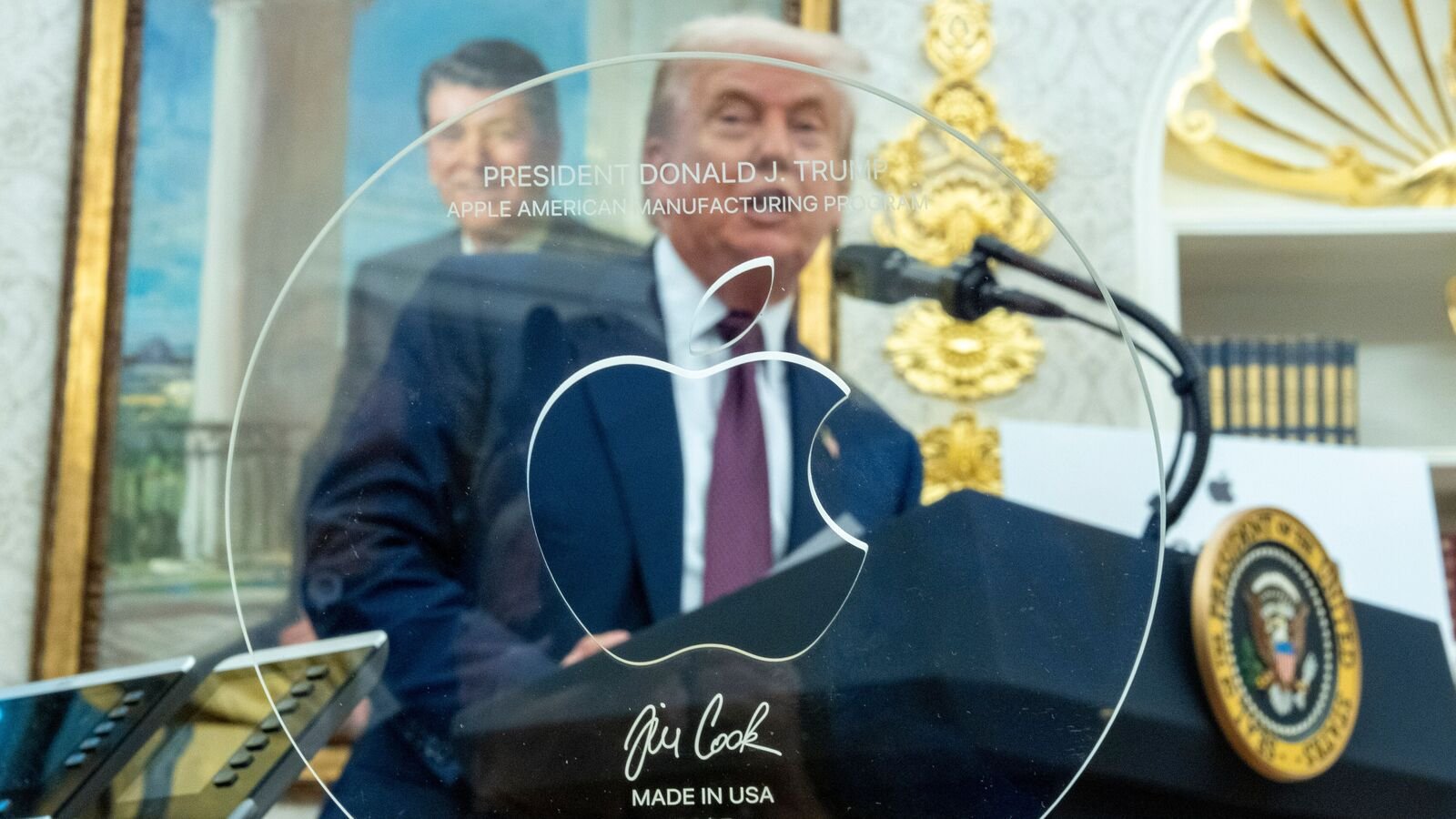 President Donald Trump is seen through a gift given to him by Apple CEO Tim Cook in the Oval Office of the White House, Wednesday, Aug. 6, 2025, in Washington. (AP Photo/Alex Brandon)