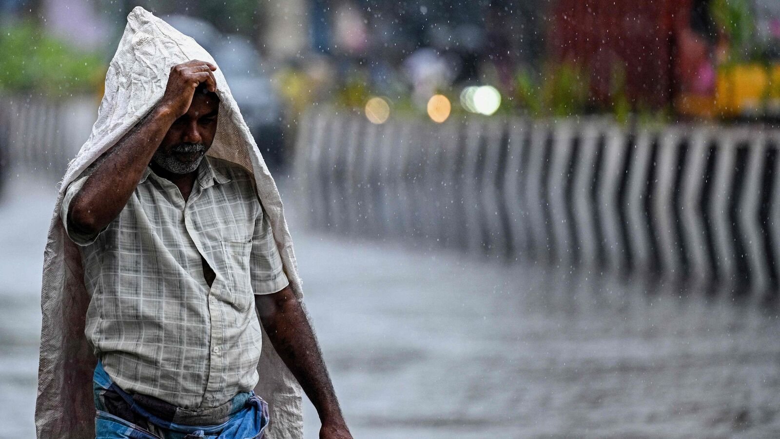 A man takes cover under a plastic sheet as he walks along a street during rainfall in Chennai