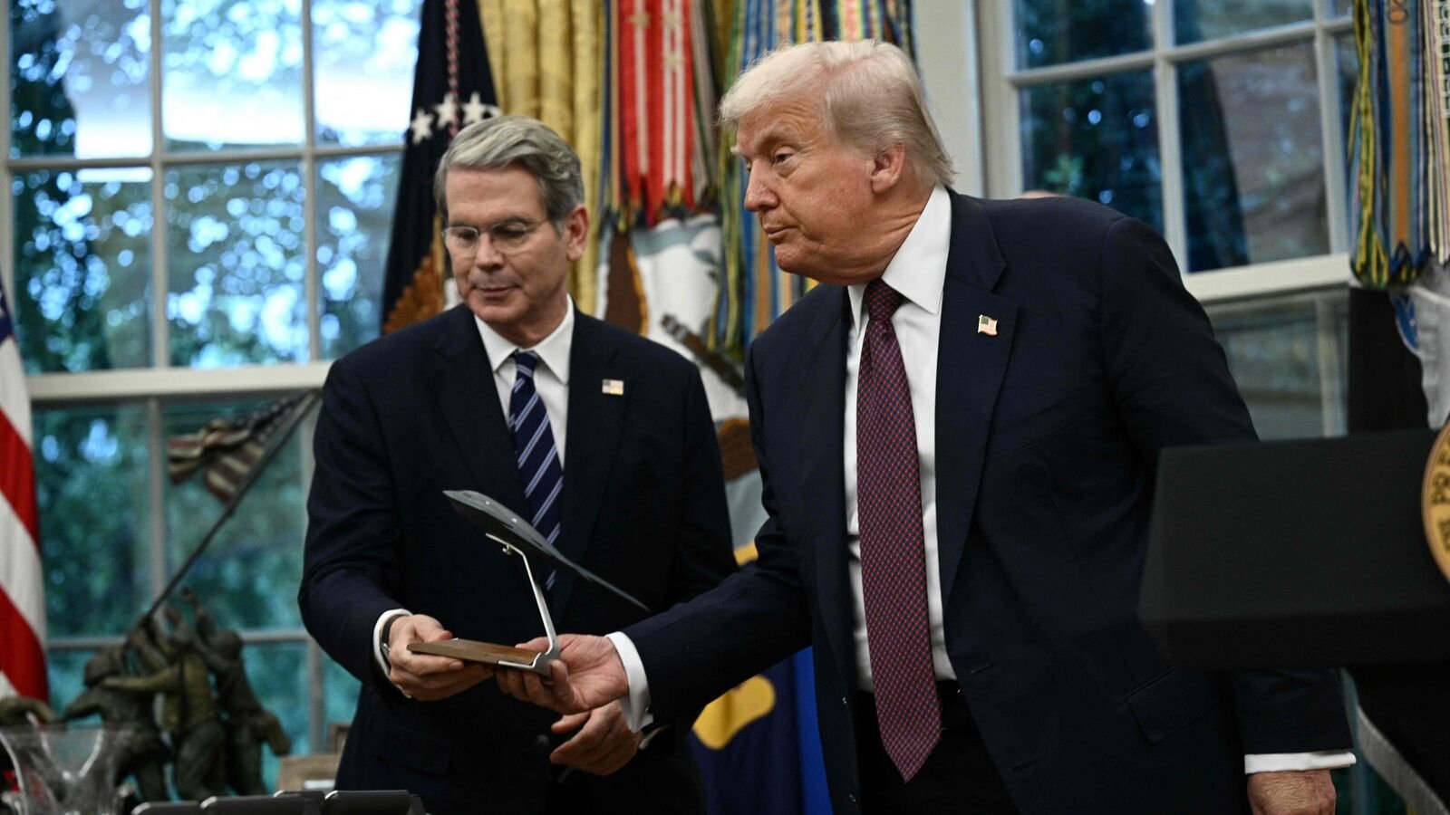 US President Donald Trump hands Treasury Secretary Scott Bessent a model of a new version the B-2 stealth bomber as he speaks in the Oval Office of the White House in Washington, DC, on August 6, 2025 to announce Apple will invest an additional $100 billion in the United States, taking its total pledge to $600 billion over the next four years. (Photo by Brendan SMIALOWSKI / AFP)