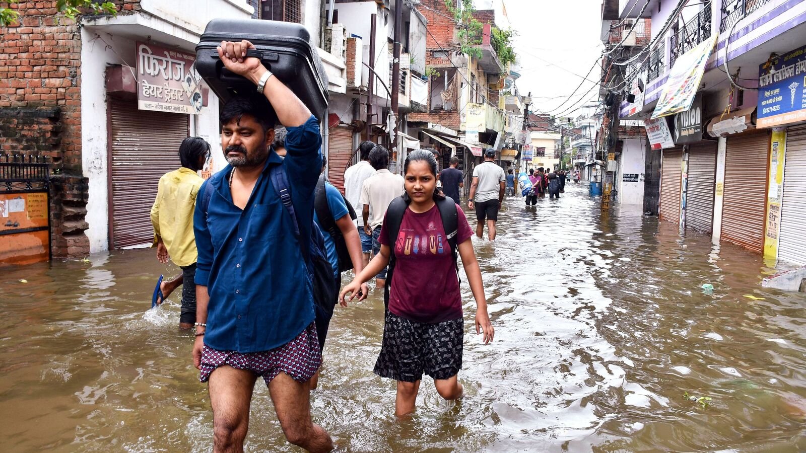 UP rains: Residents wade through a flooded street carrying their belongings after heavy rains in Prayagraj on Sunday, August 3.