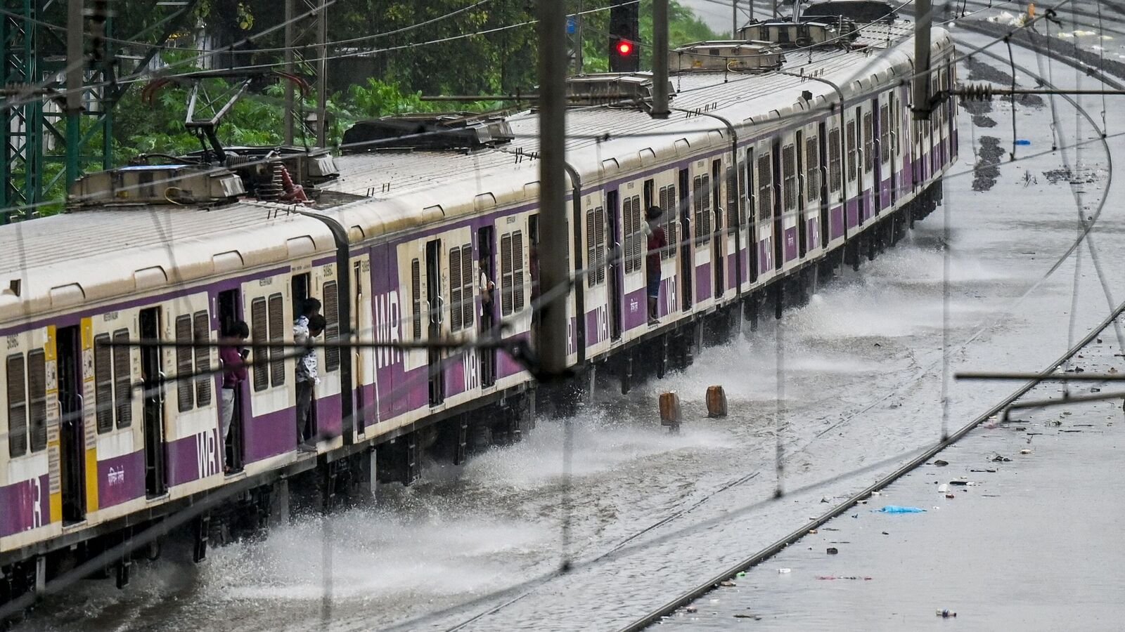 A local train rides through a flooded railway track during heavy rain showers in Mumbai on August 18, 2025. (Photo by Punit PARANJPE / AFP)