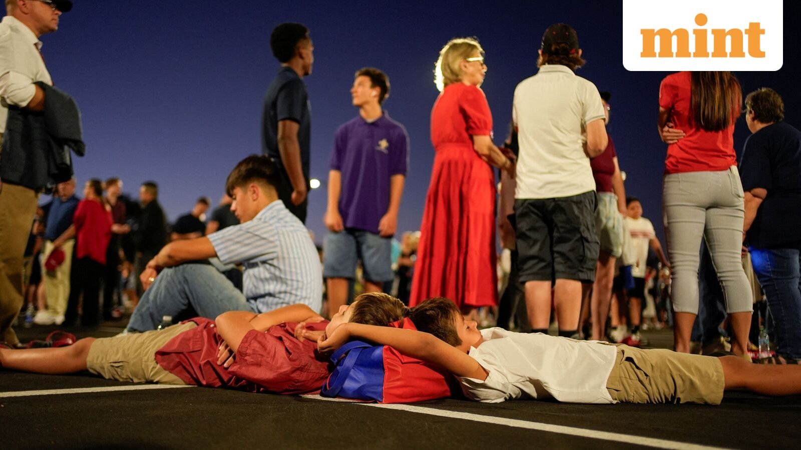 Children wait, lying on the ground before daylight, to attend a memorial service for slain conservative commentator Charlie Kirk at State Farm Stadium, in Glendale, Arizona, U.S., September 21, 2025.  REUTERS/Cheney Orr