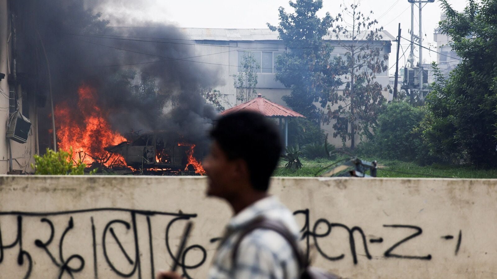 A demonstrator walks past a burned vehicle at the office of the Communist Party of Nepal (Unified Marxist-Leninist) led by the KP Sharma Oli, who resigned as Nepal's Prime Minister.