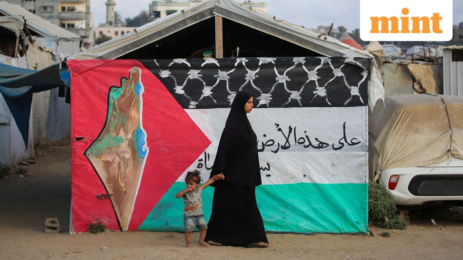 A displaced Palestinian woman walks with a child past a Palestinian flag at the Bureij camp for refugees in the central Gaza Strip on September 22, 2025. Britain, Australia, Canada and Portugal recognised the State of Palestine on September 21, a historic shift in decades of Western foreign policy that drew swift anger from Israel and a rebuke from the United States. (Photo by Eyad BABA / AFP)